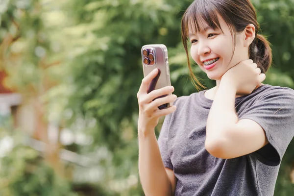 Asian woman is holding a phone to use social media or communicate online with a cheerful face with a natural background.