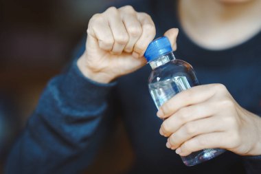 Su şişesini açan kişi, yakın planda el ve şişe çekimine odaklanmış. Temiz içme suyuyla sulanmaya devam et..