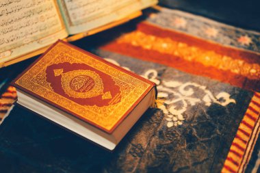 Kuran, İslam 'ın kutsal kitabı, burada bir dua paspasında dinlenirken resmedilmiştir. Kitap, Arapça yazılmış bir sayfayı açıyor..