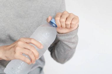 Gri gömlekli adam plastik bir şişe su açıyor. Kapağı bükülen, soğuk içecekle sulandırmaya hazır ellerin yakın çekimi..