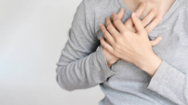 Крупным планом изображение человека в серой рубашке с руками на груди, показывающее эмоциональный или сердечный жест.