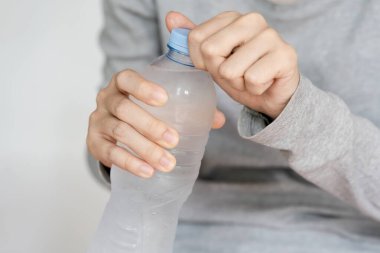 Plastik bir su şişesi açan bir kişi, günlük hayatta su ve kolaylığı vurguluyor..