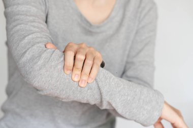 Koluna nazikçe masaj yapan birinin yakın plan görüntüsü kas gerilimi ya da ağrıdan kurtulduğunu gösteriyor. Kişi gri uzun kollu bir gömlek giyiyor..