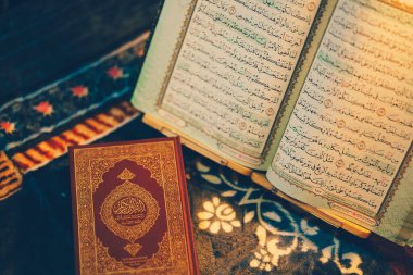 Dekoratif yüzeyde duran karmaşık Arapça harflerin yer aldığı güzel bir şekilde açılmış dini kitap. Sayfalar zarif kaligrafi, düşünce ve yansımayı davet eder.