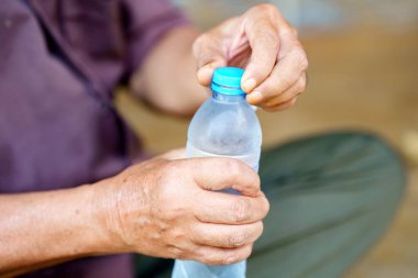 İki eliyle plastik su şişesini açan kişi, aksiyona ve şişenin dokusuna odaklanıyor. Sahne ferahlatıcı ve susuz kalma anını öneriyor..