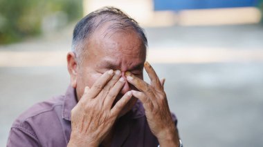 Yaşlı bir adam gözlerini oyarken derin duygular ifade eder, üzüntü ve üzüntü hisseder. Elleri yaşlılık belirtileri gösteriyor, deneyimleri yansıtıyor..