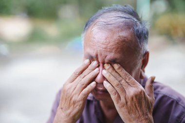 Acılı ifadeye sahip bir adam elleriyle gözlerini kapatırken, üzüntü ve üzüntü hissederken görülüyor. Geçmişi bulanık, duygusal durumuna odaklanmış..