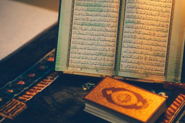Güzel bir şekilde açılmış dini kitap dekoratif yüzeyde duruyor. Yanında da daha küçük kitap ve dua boncukları var. Huzurlu ve düşünceli bir atmosfer yaratıyor..
