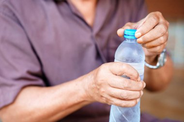 Plastik su şişesini açan kişi, ellerine ve şişesine odaklanmış. resim günlük ayarlarda eylem yakalar, şişe ve insan elinin dokusu vurgulanır.
