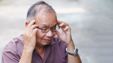 Gözlüklü yaşlı bir adam, sıkıntılı bir düşünceyi düşünürken başını tutarak stres ya da rahatsızlık hissediyor gibi görünüyor..