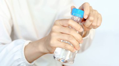 Bir adam bir şişe su açıyor, mavi şapkayla şişeyi tutan elleri gösteriyor..