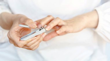 Tırnak makasıyla tırnak makasıyla yakın plan çekilen eller, kişisel hijyene önem vermek ve tarafsız bir arkaplanda bakım yapmak..