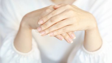 Nazikçe yerleştirilmiş ellerin yakın çekimi, yumuşak, narin bir görünüm sergiliyor, açık ten tonlarıyla nötr bir arkaplana karşı..