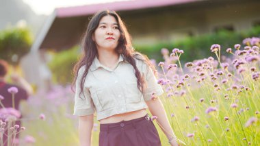 Genç bir kadın, hayat dolu bir çiçek tarlasında yürüyor. Doğanın güzellikleriyle çevrili güneş ışığında neşe saçıyor..