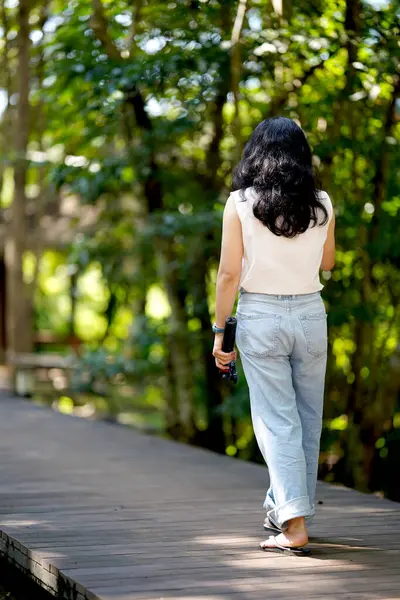 Bir kadın yemyeşil yemyeşil bir yolda yalınayak yürüyor, doğanın huzurunun tadını çıkarıyor..