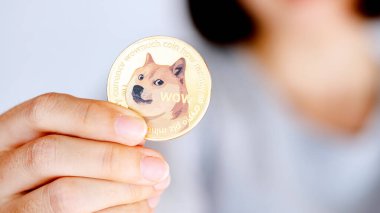 Bir kişi, kripto para birimi ya da dijital para birimi kültürünü temsil eden bir köpek grafiği içeren bir altın sikke tutuyor..