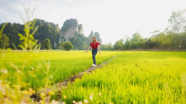 Genç bir kadın canlı yeşil pirinç tarlalarında geziniyor, parlak bir gökyüzünün altındaki yüksek dağlarla çevrili, doğadaki huzurlu bir anı yakalıyor..