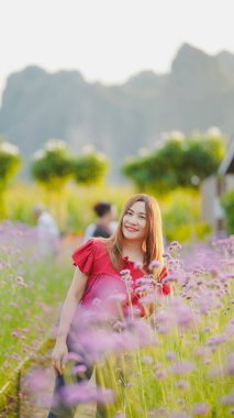 Rengarenk çiçeklerin arasında gülümseyen bir kadın. Arka planda dağlar, huzurlu ve neşeli bir atmosfer yaratıyor..