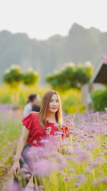 Kırmızı bluzlu bir kadın canlı mor çiçeklerin arasında duruyor, güneşli bir günün tadını çıkarıyor..