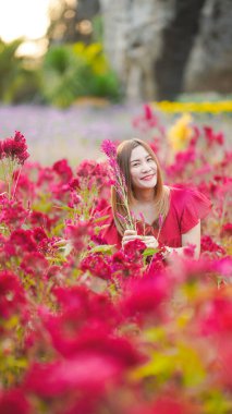 Bir kadın canlı kırmızı çiçeklerin arasında otururken ışıl ışıl gülümsüyor..