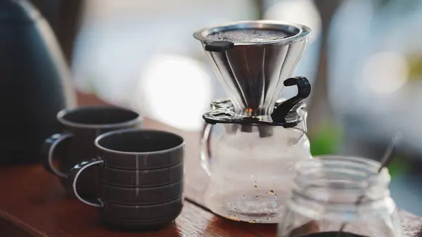 Dökümcü, cam kap ve koyu bardaklardan oluşan bir demleme kahve seti, rahat bir atmosfer yaratıyor..