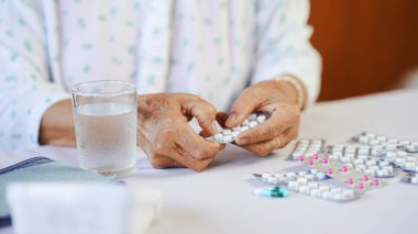 Yaşlı bir insan elinde bir paket ilaç, masada bir bardak su, sağlık sigortası konsepti...