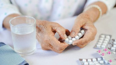 Yaşlı bir insan elinde ilaç paketi, masada bir bardak su, sağlık sigortası konsepti