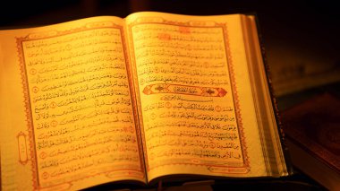 Karmaşık Arapça metin ve dekoratif sınırlar içeren açık kutsal Kur 'an İslam bağlılığını simgeleyen sıcak ışıkla aydınlatılmış.
