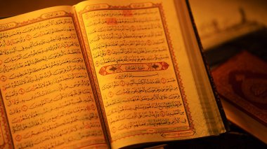 Kuran 'ı sıcak aydınlatma altında sergilenen, inanç ve maneviyatı simgeleyen süslü bir yazıyla aç.