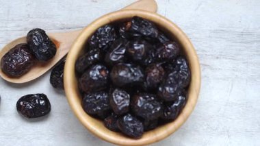 Kurumuş siyah hurma meyvesi ahşap kasede ve kaşıkla açık tahta yüzeyde doğal dokuyu ve zengin rengi gösteriyor.