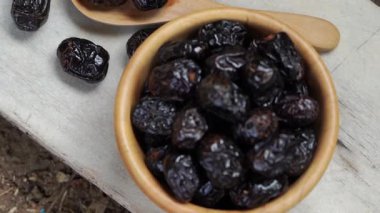 Kurumuş siyah hurma meyvesi ahşap kasede, ahşap kaşıkla kırsal masada doğal dokuyu ve zengin rengi gösteriyor.