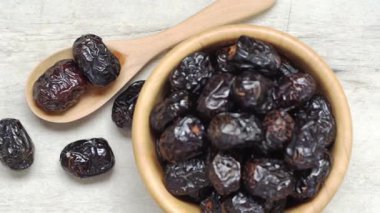 Kurumuş siyah zeytin ve ahşap kasede, hafif yüzeyde tahta kaşıkla, doğal besin dokusunu ve sağlıklı atıştırmalıkları gösteren hurmalar.