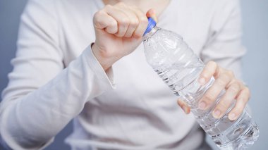 Mavi kapaklı, berrak plastik su şişesini açan biri, ellerinizi kapatın, hidrasyon konsepti, günlük ev dekorasyonu.