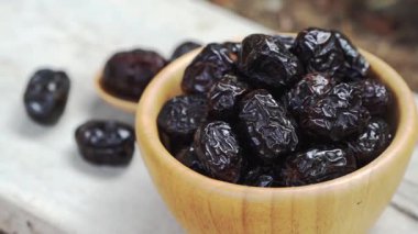 Kırsal yüzeyde ahşap kasede kurumuş siyah tarih meyvesi, kırışık bir doku ve zengin renkli atıştırmalık.