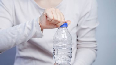 Temiz plastik su şişesini açan biri, el bükücü mavi başlık, günlük beyaz gömlek, hidrasyon konsepti, kapat.