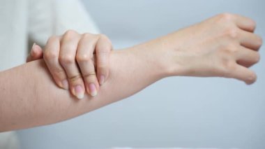 Asyalı bir kadın kendi koluna odaklanmış bir ifadeyle masaj yapıyor. Tarafsız arka plan karşısında günlük kıyafetler giyiyor. Kişisel bakım ve kas gevşemesini gösteriyor..