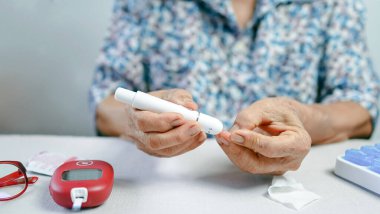 Beyaz masadaki diyabet izleme araçlarını kullanarak evdeki kan şekerini ölçmek için kıdemli eller mızrak aletini parmağına batırıyor..
