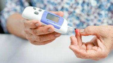 Ev ortamında diyabet kontrolünü temsil eden kan şekeri testi için parmağına iğne batıran ve dijital glukometre kullanan yaşlı kişi.