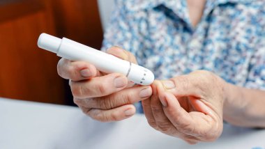 Evde kan şekeri seviyesini ölçmek, eller ve tıbbi cihazlara odaklanmak, diyabet yönetimi ve sağlık hizmetleri rutinini vurgulamak için kan şekeri ölçer kullanan yaşlı bir kişi