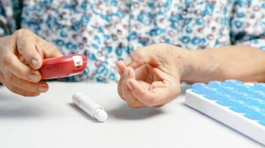Şeker seviyesini ölçmek için kan şekeri ölçer kullanan yaşlı bir kişi, evde diyabet yönetimi, ellerin kapatılması, sağlık ve tıbbi konsept