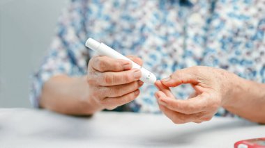 Evde şeker seviyesini kontrol etmek için kan şekeri ölçer kullanan yaşlı kişi, el ve cihaza, diyabet yönetimi, sağlık hizmetleri ve kendini izleme kavramına odaklanıyor.