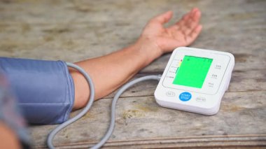 Tahta bir masada yeşil ekranlı dijital tansiyon monitörü kullanan bir kişinin yakın plan fotoğrafı, tıbbi, sağlık, kalp sağlığı ve sağlıkla ilgili içerik için ideal.