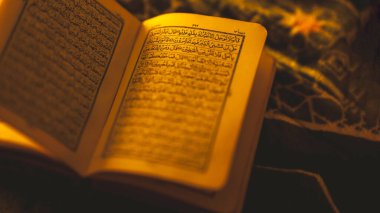Sıcak altın ışıkla aydınlatılmış Arapça kaligrafi ile açık Kur 'an, Ramazan boyunca İslam inancını, ruhaniliği, duayı ve bağlılığı sembolize eder..