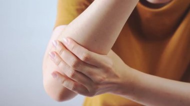 Dirseğini iki eliyle tutarak dirsek ağrısını, eklem yaralanmasını, eklem iltihabını ve sağlık hizmetleri konseptini temsil eden bir kişinin yakın çekimi..