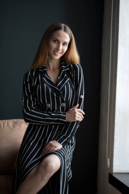 Genç, güzel esmer, siyah çizgili elbiseli, odada poz veren.