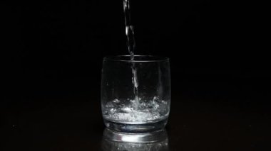 Koyu arkaplanda bardağa sıvı dökülüyor.