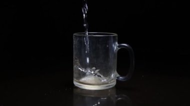 Koyu arkaplandaki şeffaf kupaya sıvı dökülüyor