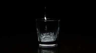 Koyu arkaplanda bardağa sıvı dökülüyor.