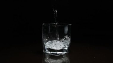 Koyu arkaplanda bardağa sıvı dökülüyor.