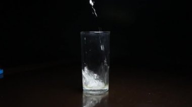 Koyu arkaplanda bardağa sıvı dökülüyor.